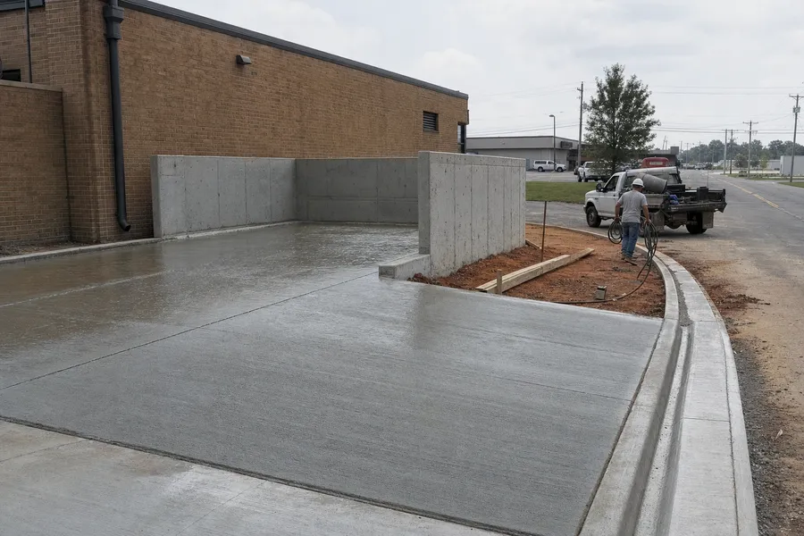 A freshly poured concrete dumpster pad and approach with new curb and gutter beside a commercial building on the US 41 strip in Henderson, Kentucky