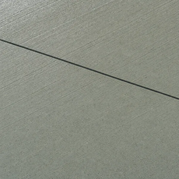 Close view of a broom-finished concrete surface crossed by a straight saw-cut control joint